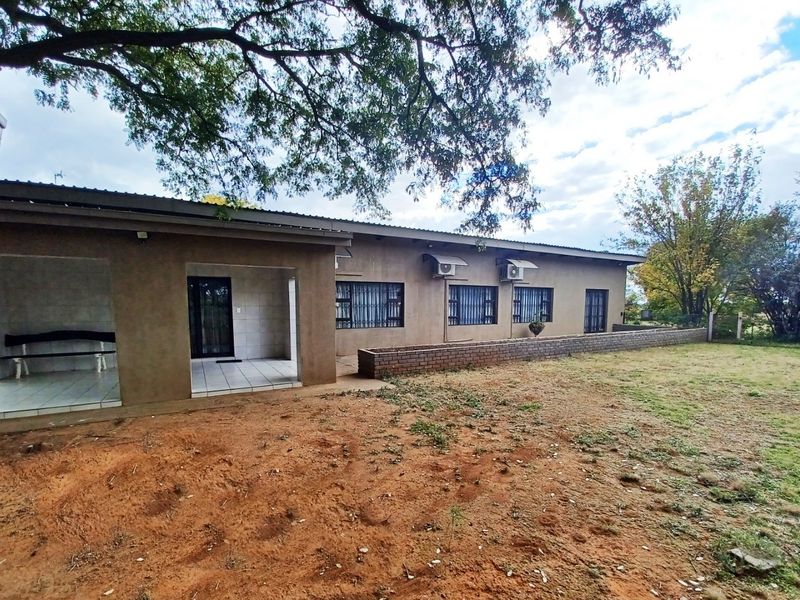 Rear view of the property featuring a covered patio, tiled flooring, security bars on windows, and a brick retaining wall set against a large garden.