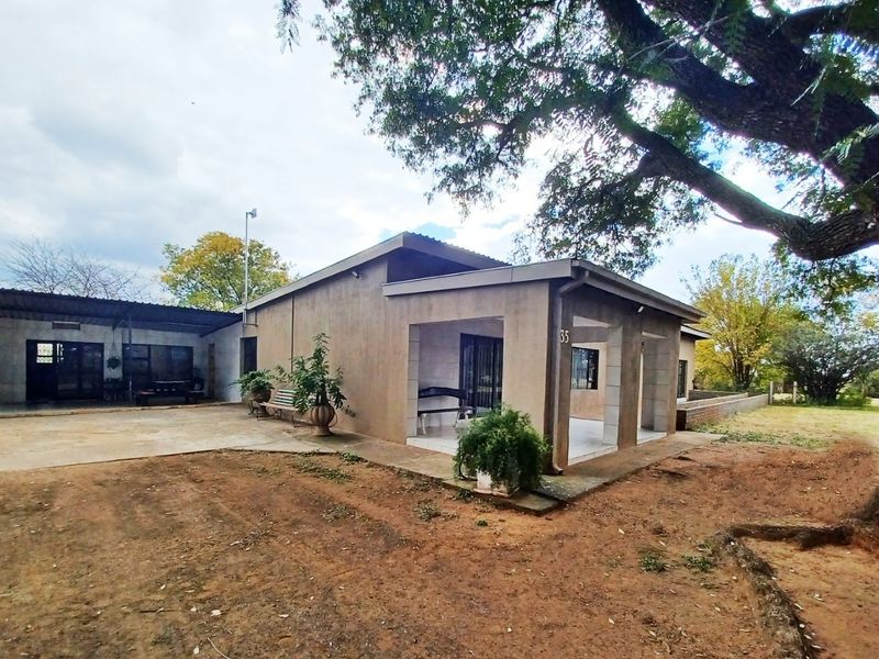 Front view of a single-story small holding residence featuring a covered patio, concrete driveway, and mature landscaping.