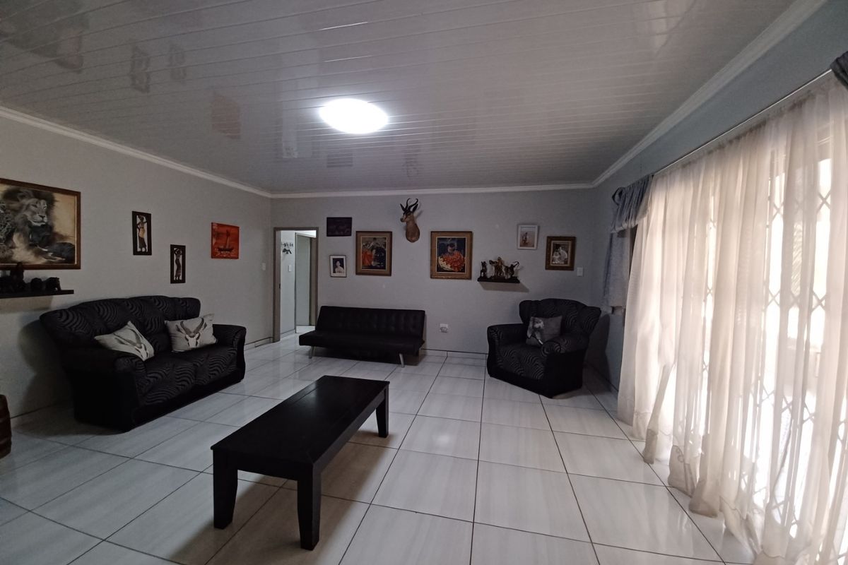 Spacious living room featuring large format floor tiles and a glossy ceiling finish, with direct access to the exterior through a sliding door.