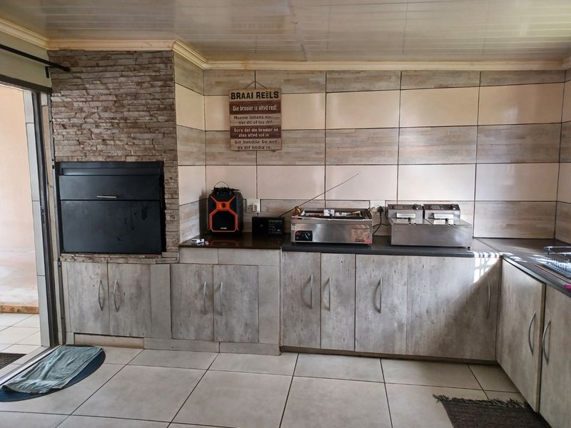 Covered patio area featuring a built-in braai with stone cladding, tiled flooring, and ample fitted cabinetry for outdoor entertainment and food preparation.