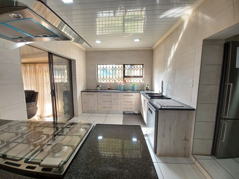 Modern kitchen featuring granite countertops, built-in cabinetry, gas hob with extractor fan, and tiled finishes, offering a clean and functional workspace.