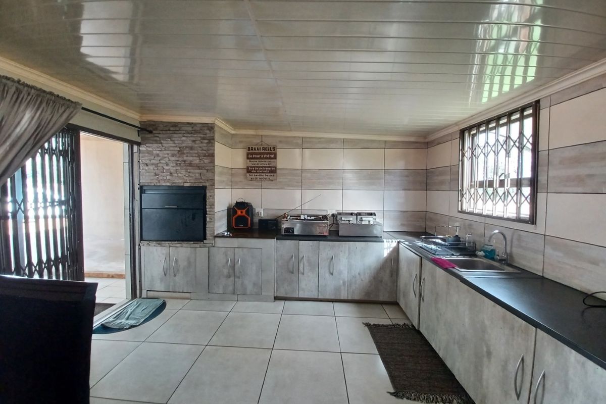 A functional kitchen featuring built-in cabinetry, a stainless steel sink, and an integrated indoor braai area with stone cladding and tiled flooring.