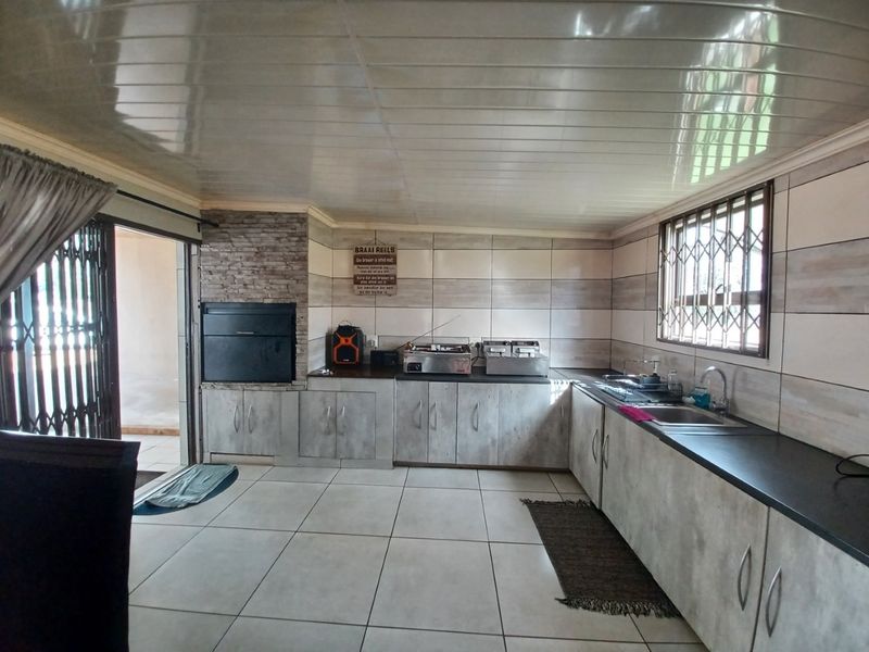 A functional kitchen featuring built-in cabinetry, a stainless steel sink, and an integrated indoor braai area with stone cladding and tiled flooring.
