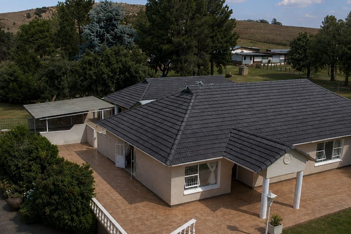 Aerial view of a farm property featuring a single-story residence with a tiled roof, expansive tiled patio area, and surrounding landscaped grounds.
