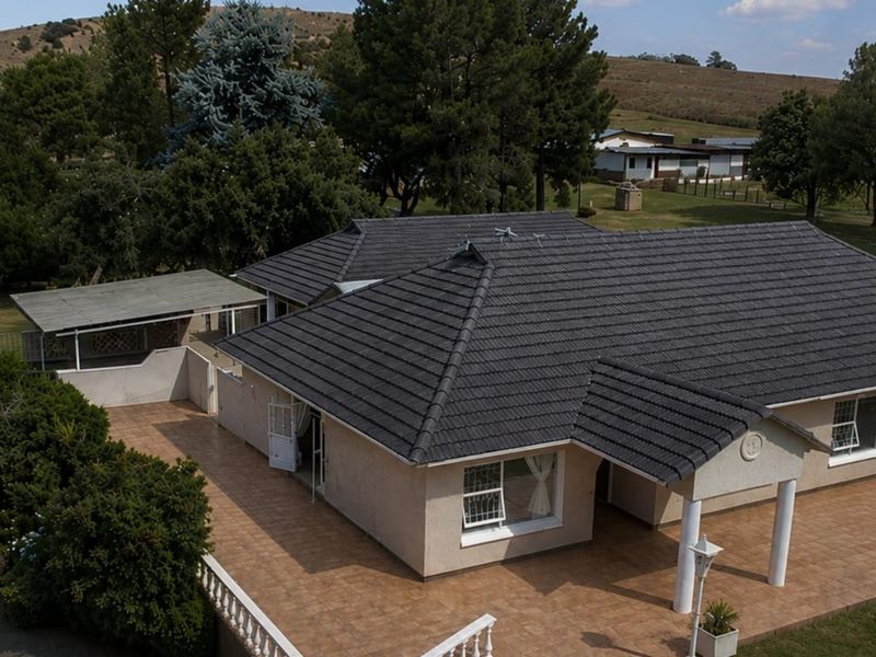 Aerial view of a farm property featuring a single-story residence with a tiled roof, expansive tiled patio area, and surrounding landscaped grounds.