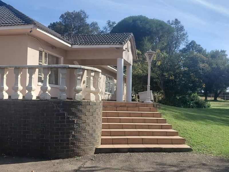 Rear exterior view of the farmhouse featuring a tiled staircase, covered porch, and a brick retaining wall with a balustrade overlooking the garden.