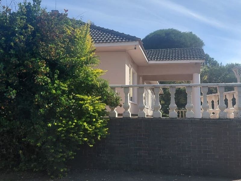Rear view of the farmhouse featuring a covered patio with a concrete balustrade, brick retaining wall, and tiled steps leading to the garden.