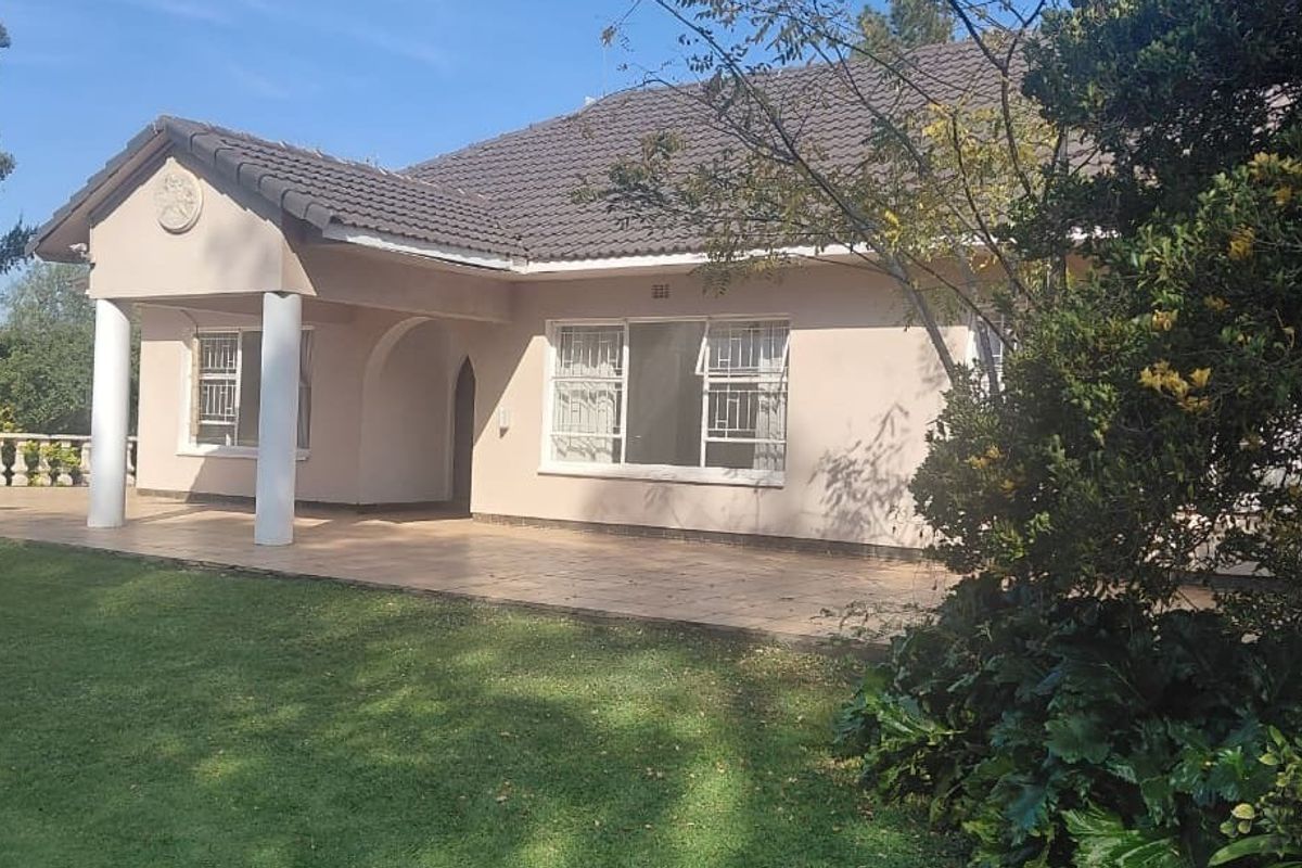 Rear view of the farm residence featuring a covered patio, tiled roof, and established garden surroundings.