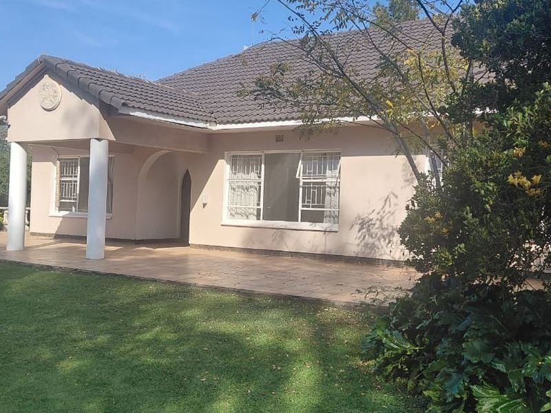 Rear view of the farm residence featuring a covered patio, tiled roof, and established garden surroundings.