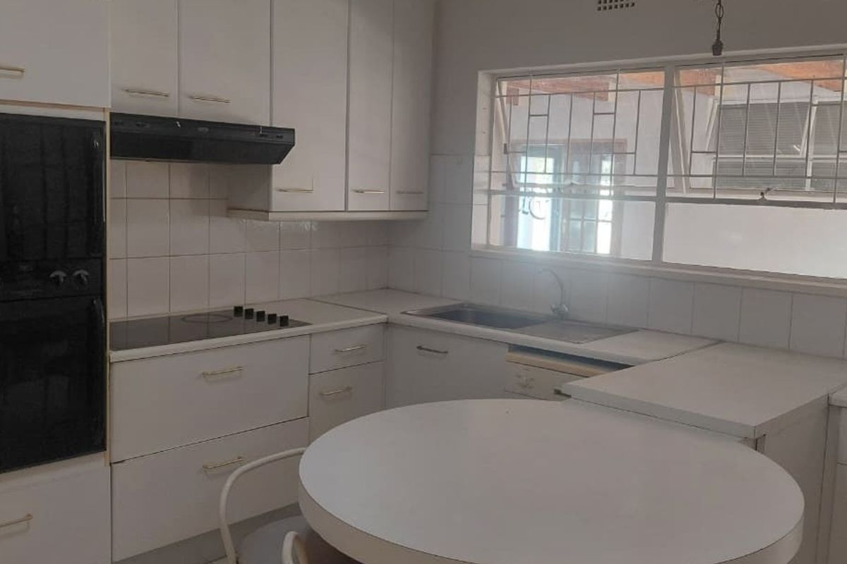 A functional kitchen featuring white built-in cabinetry, a double oven, electric hob, and a stainless steel sink with a tiled backsplash.