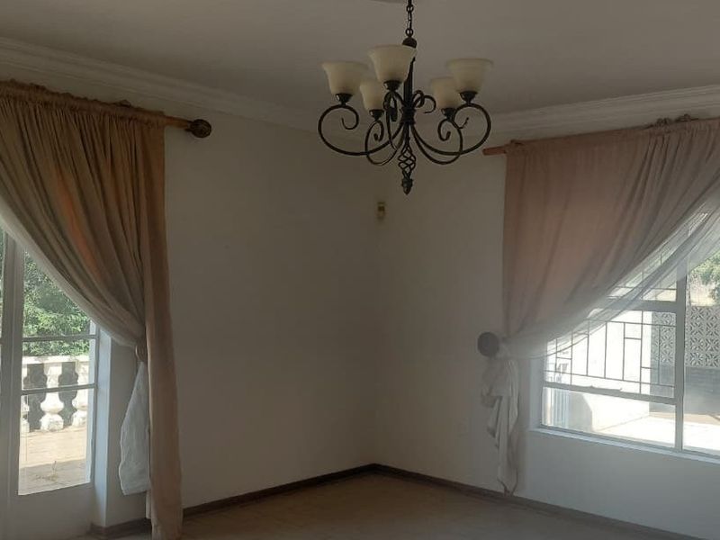 A bright, empty living room featuring tiled floors, decorative cornicing, a wrought iron chandelier, and large sliding glass doors leading to an outdoor area.
