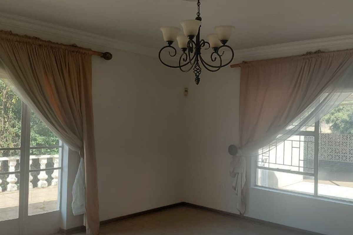 A bright, empty living room featuring tiled floors, decorative cornicing, a wrought iron chandelier, and large sliding glass doors leading to an outdoor area.