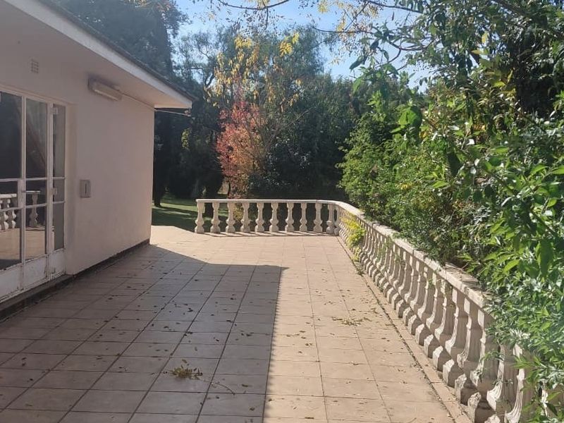 Spacious outdoor patio featuring tiled flooring and a classic concrete balustrade, overlooking the surrounding garden area.