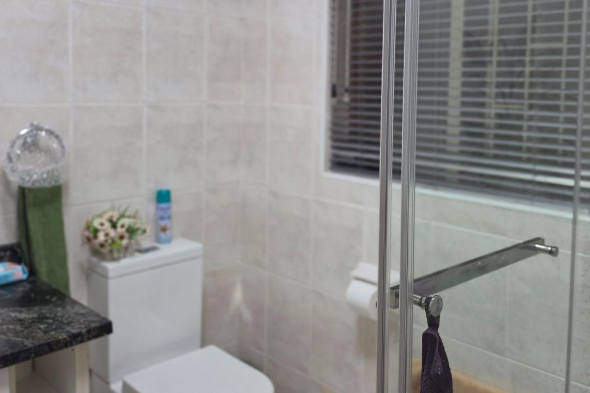 A functional bathroom featuring a vanity with a granite countertop, a toilet, and a glass-enclosed shower area with neutral wall tiling.