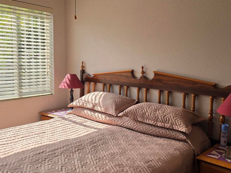 A bedroom featuring a window with fitted venetian blinds, providing natural light and a neutral wall finish.