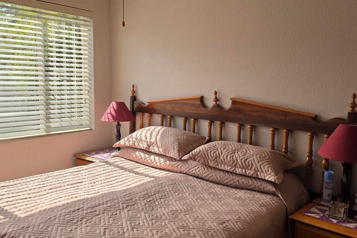 A bedroom featuring a window with fitted venetian blinds, providing natural light and a neutral wall finish.