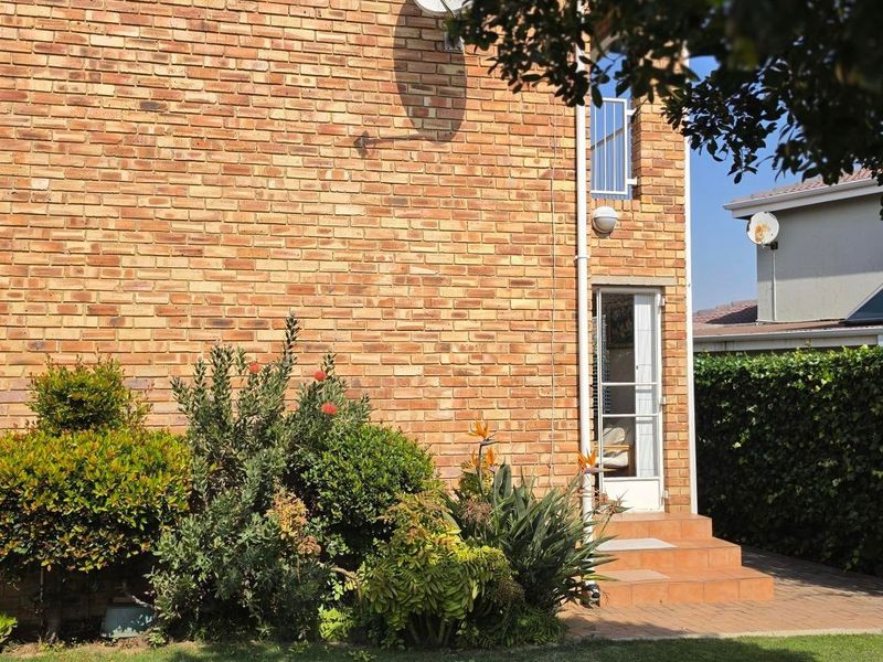 Rear view of the property featuring a face brick facade, tiled entrance steps, and established garden landscaping.