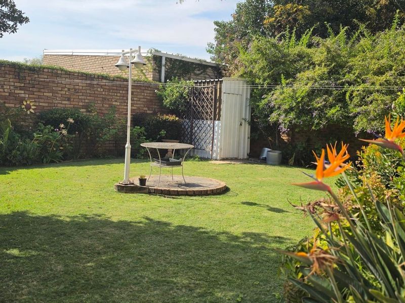 A private rear garden featuring a lush lawn, established perimeter brick wall, paved circular seating area, and a functional metal storage shed.