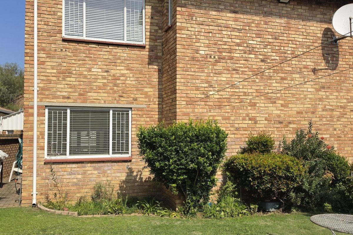 Rear exterior view of the property featuring a face brick facade, established garden beds, and a well-maintained lawn area.
