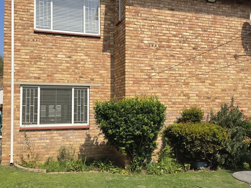Rear exterior view of the property featuring a face brick facade, established garden beds, and a well-maintained lawn area.