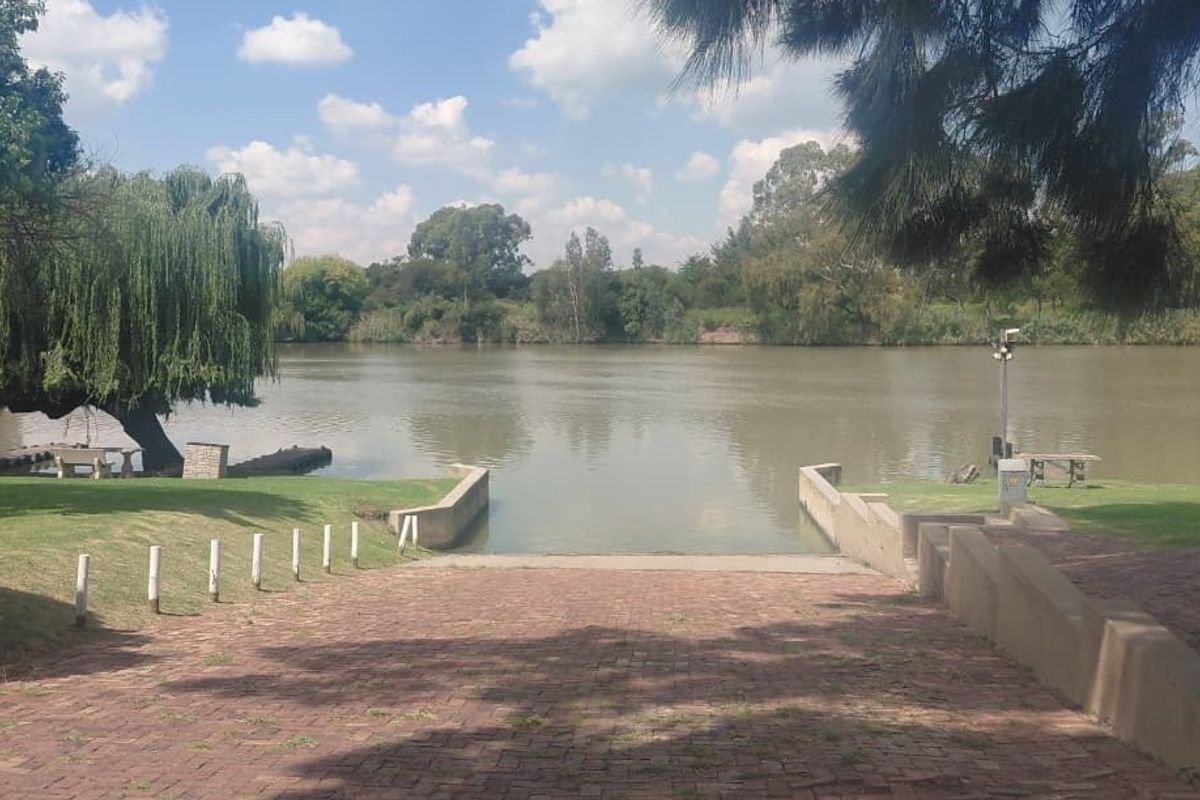 A scenic view of a riverfront property featuring a paved boat ramp, retaining walls, and well-maintained lawn area leading to the water.