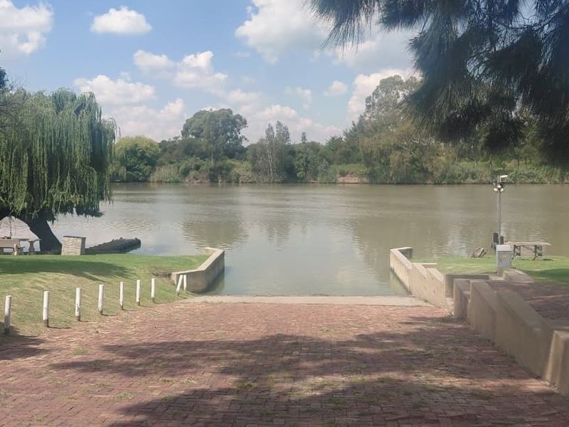 A scenic view of a riverfront property featuring a paved boat ramp, retaining walls, and well-maintained lawn area leading to the water.
