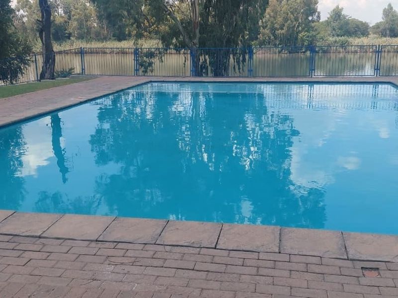 A well-maintained swimming pool area featuring paved surrounds and secure metal perimeter fencing, overlooking a tranquil water feature.