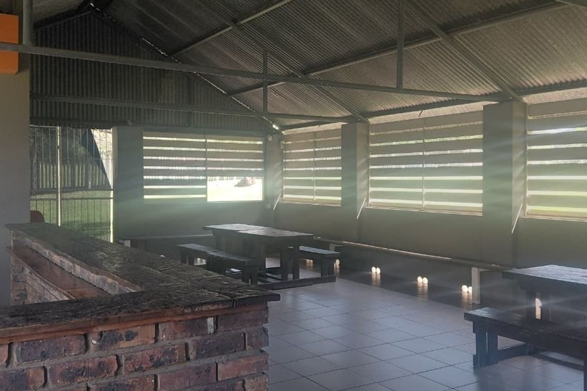 A spacious covered outdoor patio area featuring a built-in brick bar counter, tiled flooring, and roller blinds, ideal for entertaining.