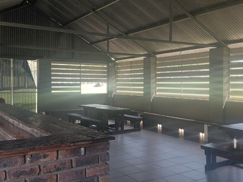 A spacious covered outdoor patio area featuring a built-in brick bar counter, tiled flooring, and roller blinds, ideal for entertaining.