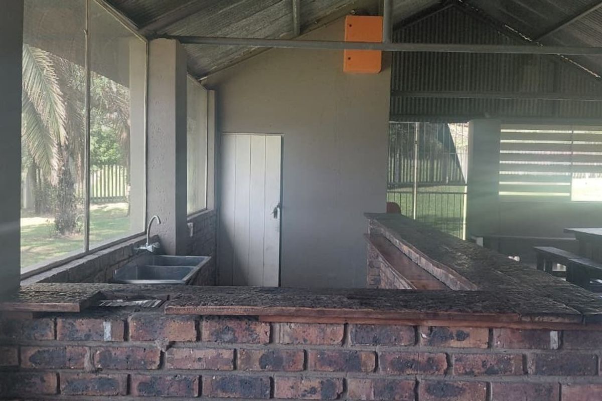 A rustic outdoor bar area featuring a brick counter, stainless steel sink, and corrugated metal roofing, offering a functional space for entertainment.