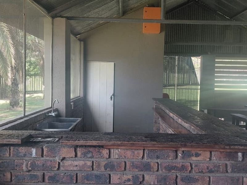 A rustic outdoor bar area featuring a brick counter, stainless steel sink, and corrugated metal roofing, offering a functional space for entertainment.