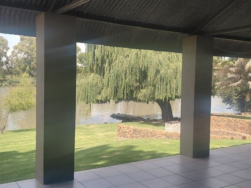 A covered patio area featuring tiled flooring and concrete pillars, offering direct views of the river and landscaped garden.