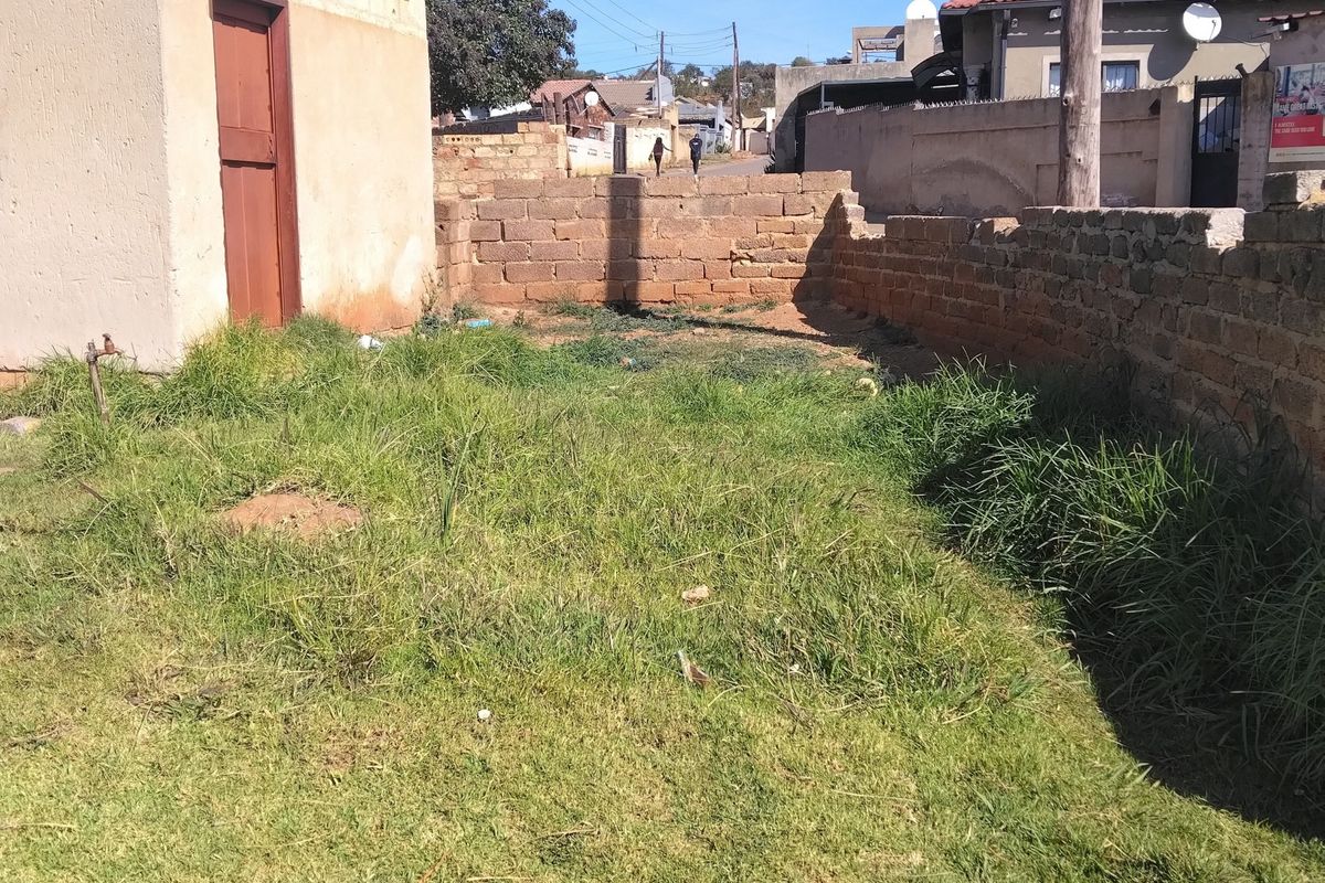 A rear yard area featuring a small outbuilding, brick boundary walls, and an overgrown lawn, offering potential for landscaping or outdoor development.