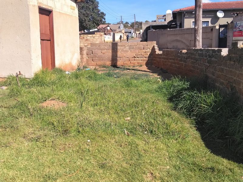 A rear yard area featuring a small outbuilding, brick boundary walls, and an overgrown lawn, offering potential for landscaping or outdoor development.