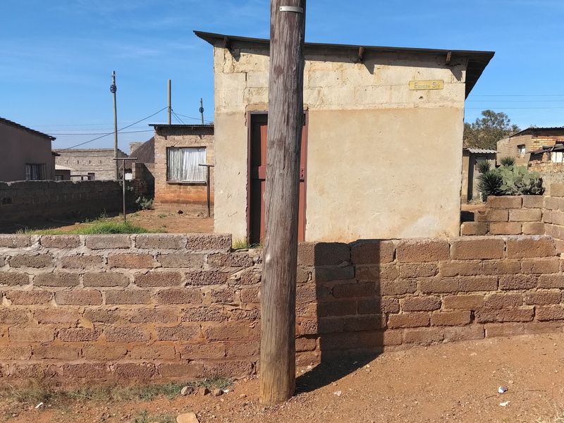 A view of a modest single-story masonry structure with a concrete block boundary wall and an adjacent utility pole.