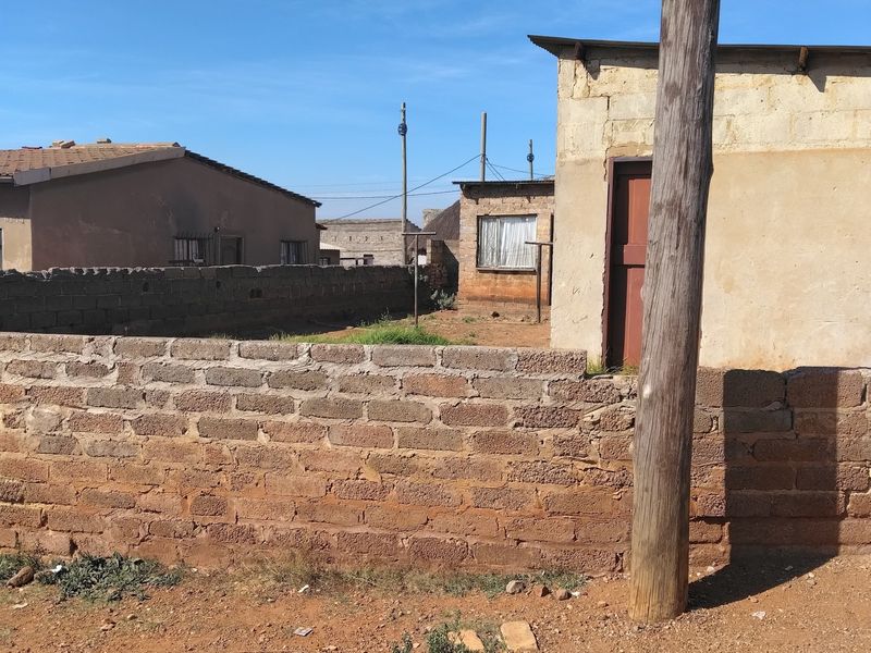View of a rear yard area featuring a masonry boundary wall and a basic single-story structure with a metal door frame.