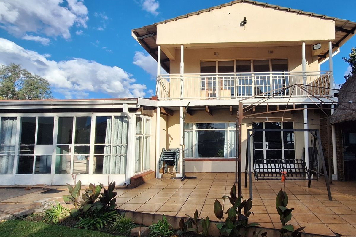 Rear view of a two-story small holding residence featuring a tiled patio, upper balcony, and extensive glass doors opening to the garden area.
