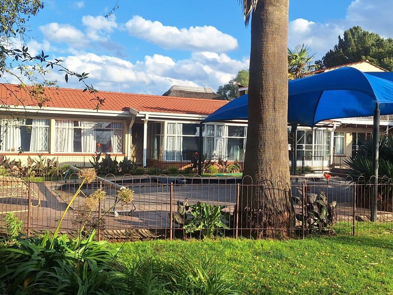Outdoor pool area featuring a tiled patio, blue shade sail, and metal perimeter fencing, set against the rear elevation of the main dwelling.