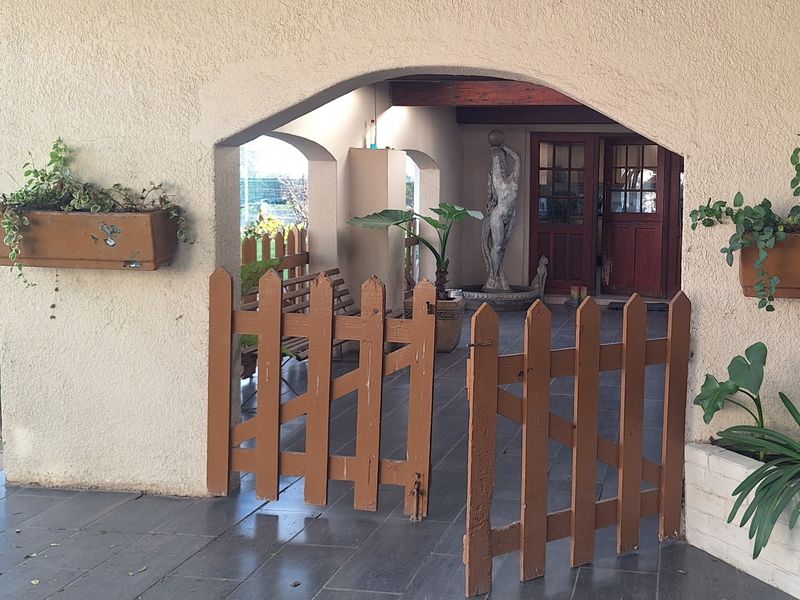 A covered patio area featuring an arched entrance, tiled flooring, and a wooden gate leading to the main dwelling entrance.
