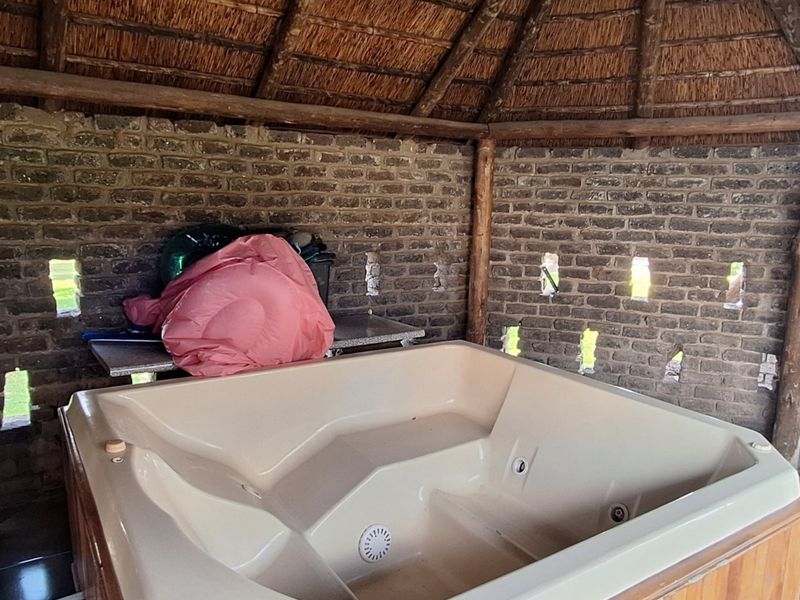 Covered outdoor spa area featuring a thatched roof, exposed brick walls, and a built-in hot tub, providing a rustic relaxation space.
