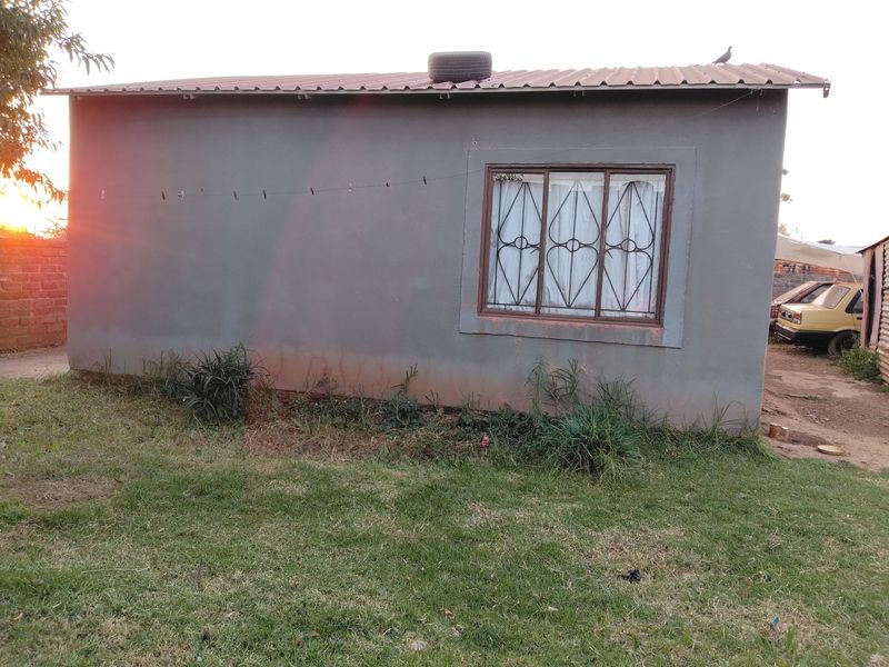 A view of the rear exterior wall of the house featuring a metal roof and a window with security burglar bars.