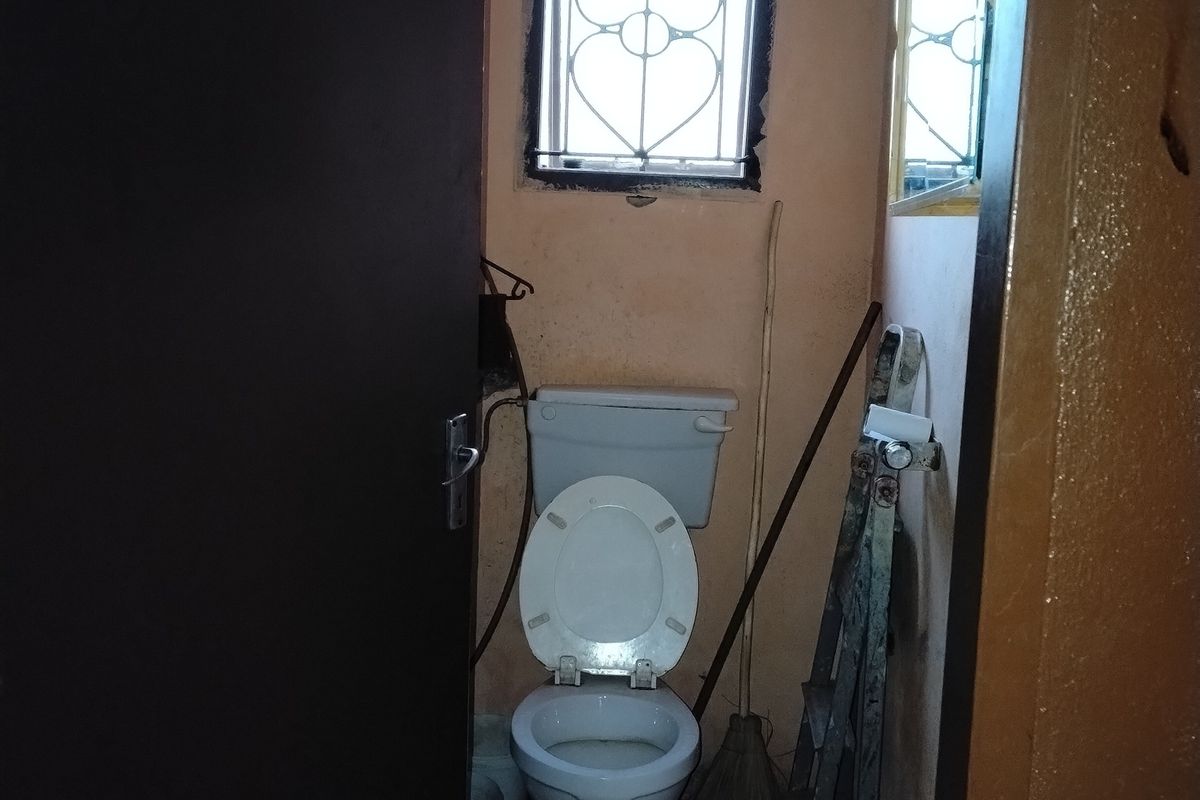 A small, dated bathroom featuring a standard toilet, tiled flooring, and a window with a security gate.