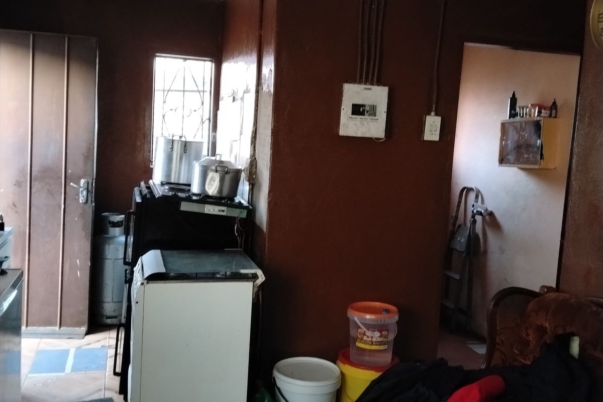A functional kitchen area featuring tiled flooring, security bars on windows, and an exposed electrical distribution board, requiring cosmetic updates to improve the space.