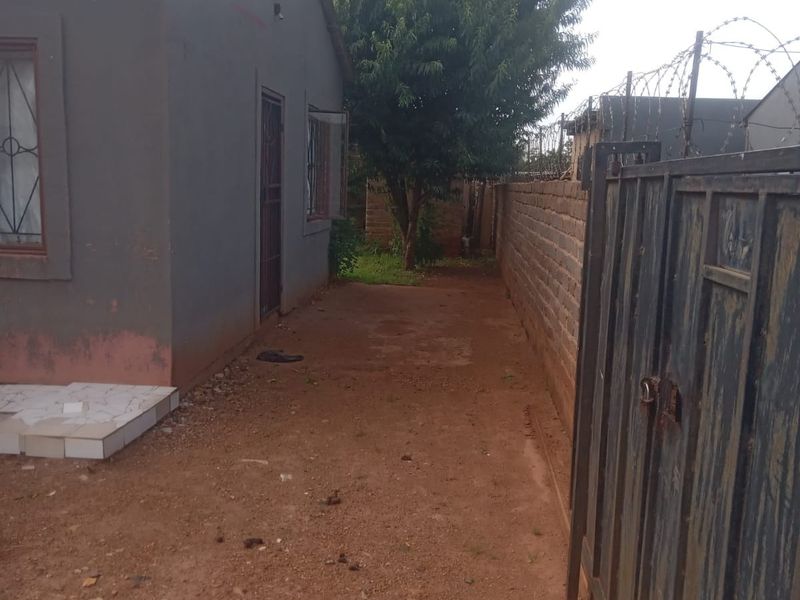 Side yard area featuring a metal security gate, brick boundary wall with razor wire, and a tiled entrance step leading to the house.