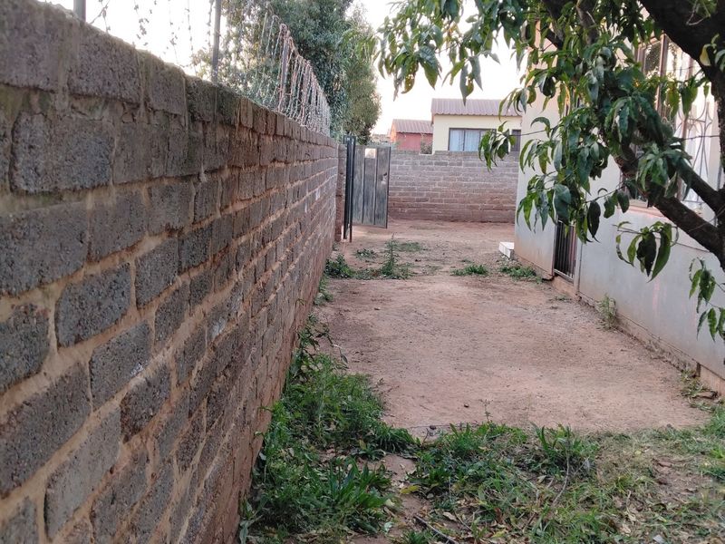 A side yard area featuring a brick boundary wall with security razor wire and an unpaved ground surface.
