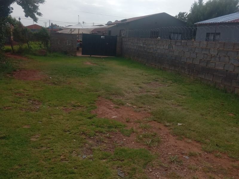 A view of the rear yard featuring a perimeter wall with security razor wire and a metal access gate.