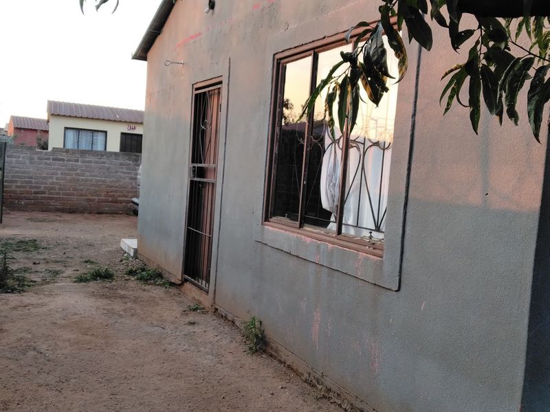 Rear exterior view of the property featuring plastered walls, metal window frames with security bars, and a security gate entrance.