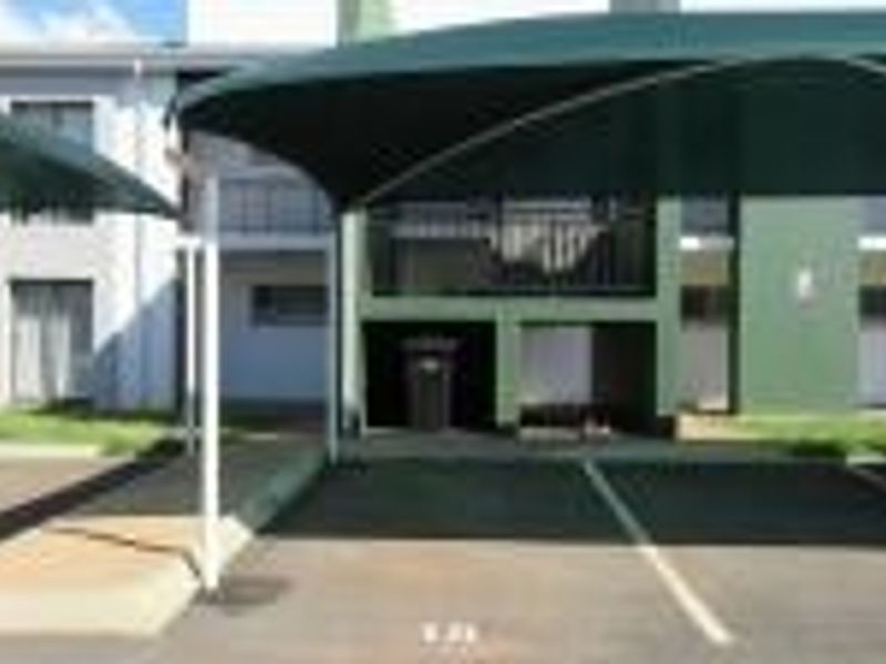 Exterior view of the apartment complex featuring designated paved parking bays with shade cloth carports.