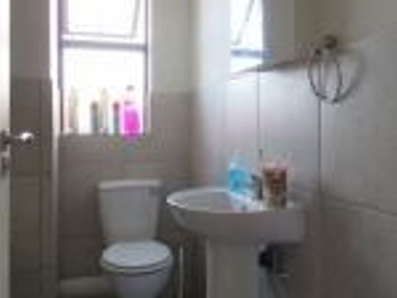 A functional bathroom featuring a pedestal basin, toilet, and neutral wall tiling, providing a clean and practical space.