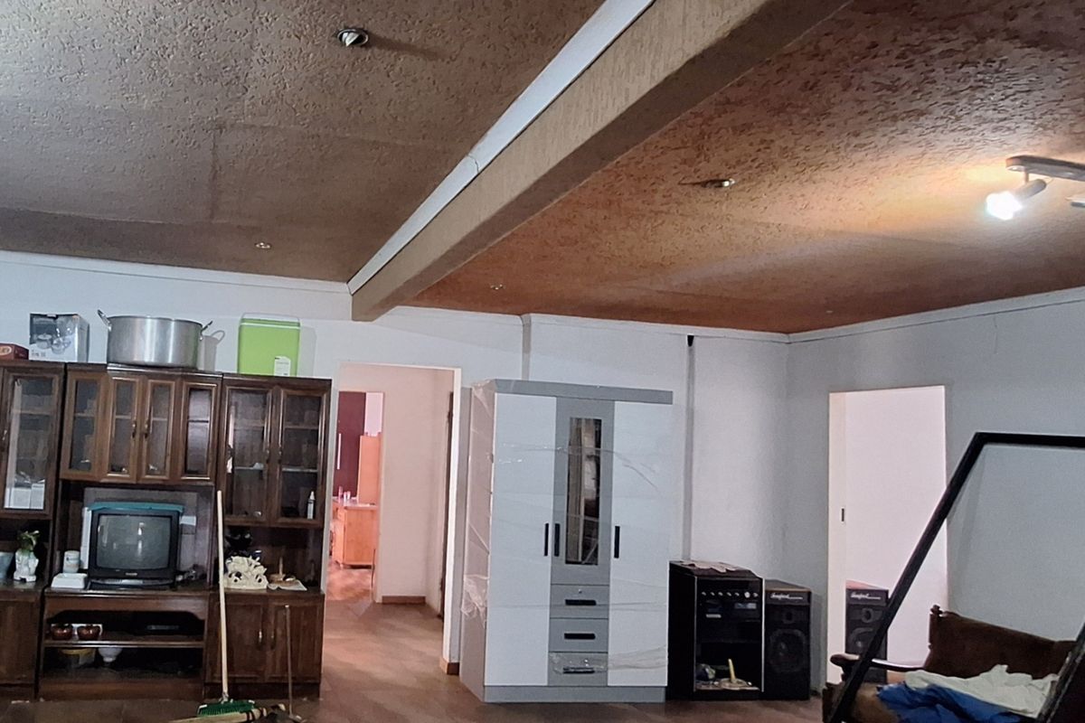 Spacious living area featuring textured ceilings with integrated lighting and laminate flooring, offering a blank canvas for renovation and modernization.